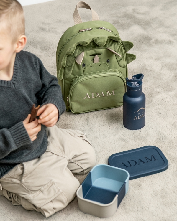 barnryggsäck i form av en dinosaurie, med broderat namn samt blå matlåda och vattenflaska